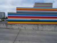 an empty parking lot painted brightly stripes on the wall of the building and sky as well as stones