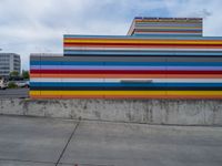 an empty parking lot painted brightly stripes on the wall of the building and sky as well as stones