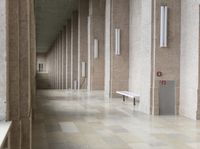 a bunch of benches in a corridor with stone walls and gray floors and grey columns