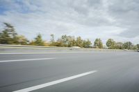 the side of a highway with cars going down it with cloudy blue sky above it
