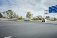 the side of a highway with cars going down it with cloudy blue sky above it