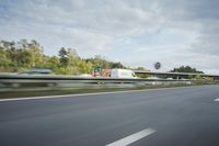 the side of a highway with cars going down it with cloudy blue sky above it
