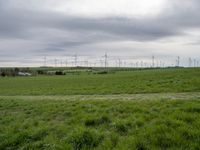 a number of different wind turbines in a field near by house under grey skies of an overcast sky