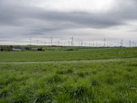 a number of different wind turbines in a field near by house under grey skies of an overcast sky