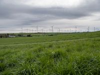 a number of different wind turbines in a field near by house under grey skies of an overcast sky