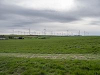 a number of different wind turbines in a field near by house under grey skies of an overcast sky