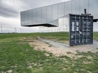 a reflection of wind turbines is in a glass wall on a grassy field by grass