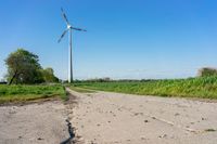 a single windmill standing on top of a green field next to a road, near a small dirt road