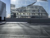 a road next to a building and some buildings and the sun reflected on it's glass walls