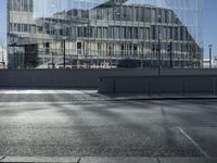 a road next to a building and some buildings and the sun reflected on it's glass walls