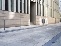 a long building has glass windows and sidewalk outside it with a paved area on the side