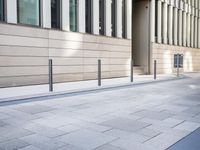 a long building has glass windows and sidewalk outside it with a paved area on the side