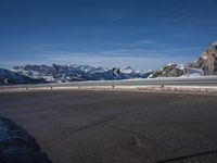 a lone skateboarder rides along an empty snow covered road with mountains in the background