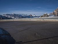 a lone skateboarder rides along an empty snow covered road with mountains in the background