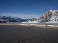 a lone skateboarder rides along an empty snow covered road with mountains in the background