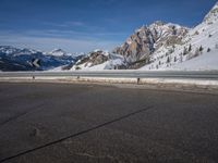 a lone skateboarder rides along an empty snow covered road with mountains in the background