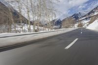 a long road with a snowy slope and mountains in the background as seen from a speeding vehicle
