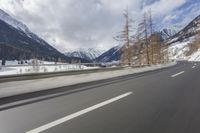 a long road with a snowy slope and mountains in the background as seen from a speeding vehicle
