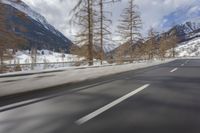 a long road with a snowy slope and mountains in the background as seen from a speeding vehicle