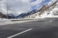 a long road with a snowy slope and mountains in the background as seen from a speeding vehicle