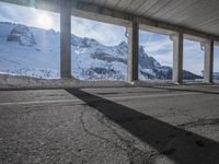 an empty parking lot next to mountains in the wintertime with a roof over and sky overhead