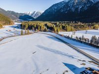 snow and a road in the middle of some mountain areas in winter time, surrounded by wooded area with large mountains