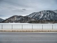 snow covering the ground with mountains in the background on a cloudy day, near an empty road and fence