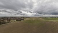 an aerial view of the landscape under grey skies and clouds with trees and farms across a farm land