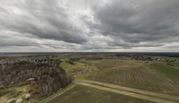 an aerial view of the landscape under grey skies and clouds with trees and farms across a farm land