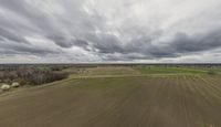 an aerial view of the landscape under grey skies and clouds with trees and farms across a farm land