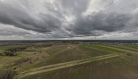 an aerial view of the landscape under grey skies and clouds with trees and farms across a farm land