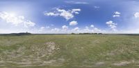 an open field with a large blue sky and white clouds above it's horizon