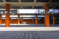 an empty parking lot with rows of orange poles, concrete pillars, and street lights