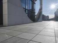 a square tile walkway is shown next to a white building with large windows and a circular design