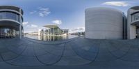 three different circular building shapes and reflections on a blue sky day with some clouds and trees