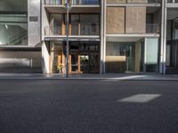 a gray building with a glass front door in the sun outside its entrance is next to an empty street
