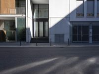 a gray building with a glass front door in the sun outside its entrance is next to an empty street