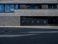 black glass window on a white brick building and street in front of it are letters that spell pier 6 and 4