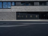 black glass window on a white brick building and street in front of it are letters that spell pier 6 and 4