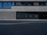 black glass window on a white brick building and street in front of it are letters that spell pier 6 and 4