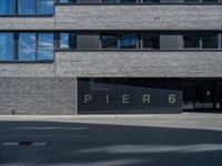 black glass window on a white brick building and street in front of it are letters that spell pier 6 and 4