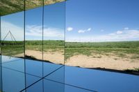 reflection of a body of water and hills in mirrors on display at a museum or cultural center