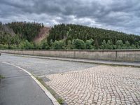 concrete walkway with trees and fenced in area on opposite sides of the road and one side of the road