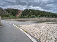 concrete walkway with trees and fenced in area on opposite sides of the road and one side of the road