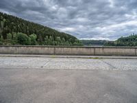 concrete walkway with trees and fenced in area on opposite sides of the road and one side of the road