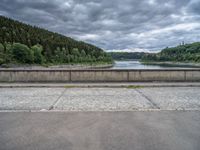 concrete walkway with trees and fenced in area on opposite sides of the road and one side of the road