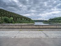 concrete walkway with trees and fenced in area on opposite sides of the road and one side of the road