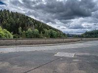 concrete walkway with trees and fenced in area on opposite sides of the road and one side of the road