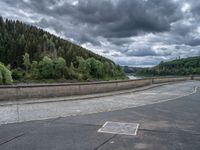 concrete walkway with trees and fenced in area on opposite sides of the road and one side of the road