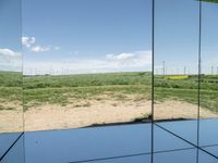 a view from inside of a glass enclosure looking out on wind turbines and the blue sky